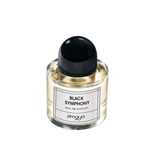 The image shows a bottle of "Black Symphony" eau de parfum by Zimaya. The perfume bottle is clear glass, filled with a pale yellow liquid. It has a sleek, modern design with a black cap and a simple white label. The label features black text that reads "BLACK SYMPHONY eau de parfum" and the brand name "zimaya" at the bottom. The overall design is minimalist and elegant, conveying a sense of sophistication and luxury.