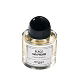 The image shows a bottle of "Black Symphony" eau de parfum by Zimaya. The perfume bottle is clear glass, filled with a pale yellow liquid. It has a sleek, modern design with a black cap and a simple white label. The label features black text that reads "BLACK SYMPHONY eau de parfum" and the brand name "zimaya" at the bottom. The overall design is minimalist and elegant, conveying a sense of sophistication and luxury.