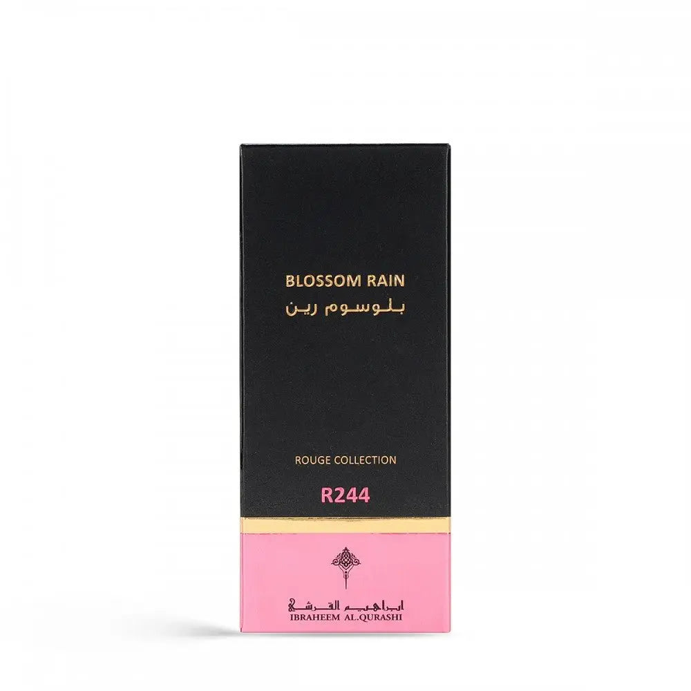 The image features a tall, narrow box for a perfume named "BLOSSOM RAIN" by Ibraheem Al Qurashi. The box has a black upper portion with the product name in gold lettering in both English and Arabic script. The lower section of the box transitions to a pink hue with "ROUGE COLLECTION" and "R244" also printed in gold, likely indicating the fragrance line and specific scent number. The brand's logo is printed near the bottom.