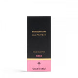 The image features a tall, narrow box for a perfume named "BLOSSOM RAIN" by Ibraheem Al Qurashi. The box has a black upper portion with the product name in gold lettering in both English and Arabic script. The lower section of the box transitions to a pink hue with "ROUGE COLLECTION" and "R244" also printed in gold, likely indicating the fragrance line and specific scent number. The brand's logo is printed near the bottom.