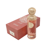 The image shows a perfume bottle named "Calabria" from the Gissah Signature Collection. The bottle is tall and cylindrical with a clear glass body that has a slight rose tint, and it is adorned with a gold ornate medallion that features intricate designs. The cap is a luxurious gold color with a decorative embossed pattern. Beside the bottle is the packaging, a box in a matching rose tint with a gold mandala design and the names "Gissah" and "Calabria" printed on it.