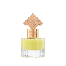 The image depicts a transparent perfume bottle with a yellow-colored liquid. The bottle is topped with a gold cap that has an ornate design, which may draw inspiration from Middle Eastern or Islamic art. The neck of the bottle features gold lettering in Arabic, likely indicating the name of the fragrance or the brand. The cap and the color of the liquid give the product a luxurious and exotic appearance, suggesting that it may be a cardamom-scented musk designed for use on hair.