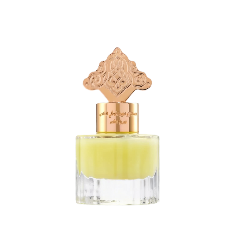 The image depicts a transparent perfume bottle with a yellow-colored liquid. The bottle is topped with a gold cap that has an ornate design, which may draw inspiration from Middle Eastern or Islamic art. The neck of the bottle features gold lettering in Arabic, likely indicating the name of the fragrance or the brand. The cap and the color of the liquid give the product a luxurious and exotic appearance, suggesting that it may be a cardamom-scented musk designed for use on hair.