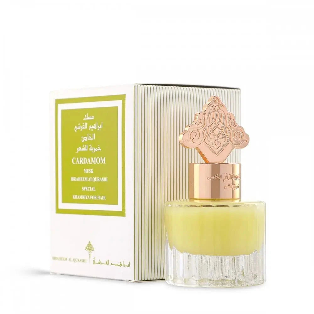 The image features a perfume bottle with a yellow-colored liquid and a decorative gold cap, accompanied by its packaging. The box has a white background with green vertical stripes on the side and a front label that reads "CARDAMOM MUSK" in English and Arabic, indicating the scent. It also says "IBRAHEEM AL.QURASHI SPECIAL KHAMRIYA FOR HAIR." The gold cap of the bottle has an intricate design, possibly inspired by Middle Eastern or Islamic art. 