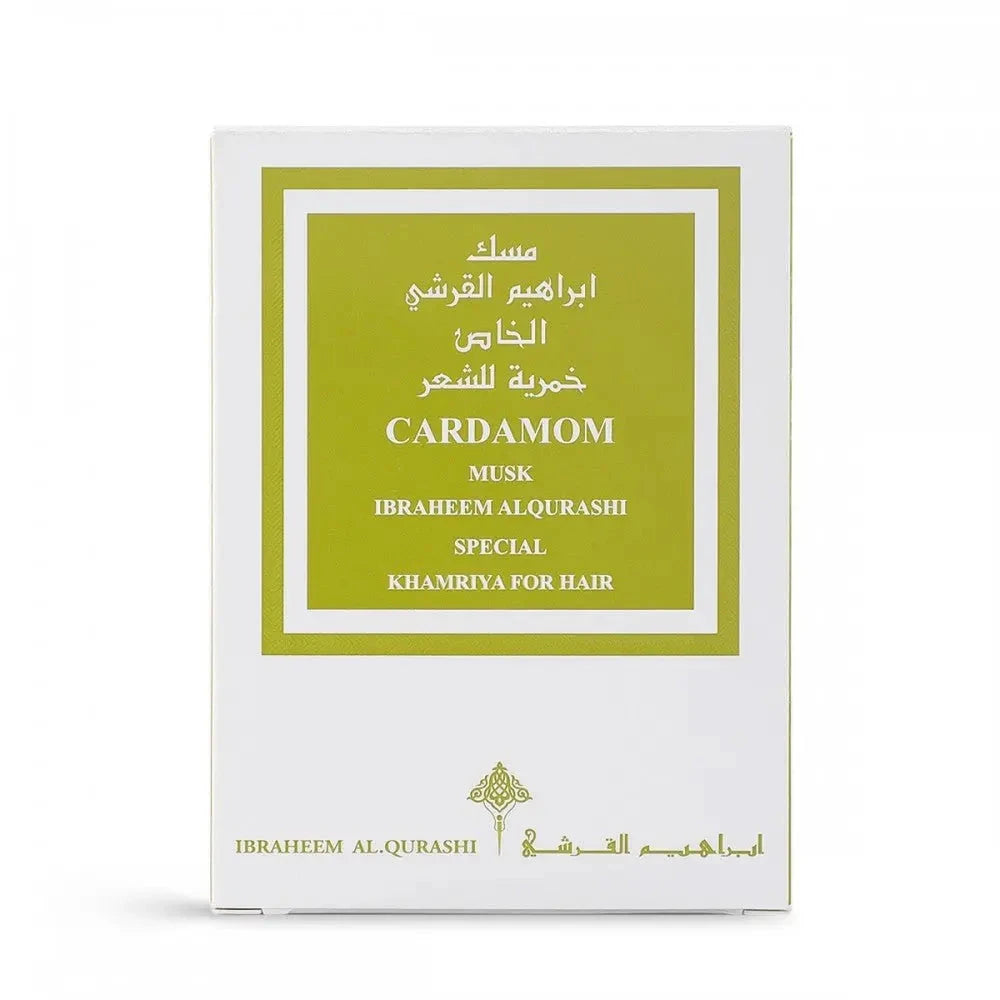 The image shows a white packaging box with a green label for a fragrance product. The label has both English and Arabic text, reading "CARDAMOM MUSK IBRAHEEM AL.QURASHI SPECIAL KHAMRIYA FOR HAIR." The design of the box is simple and elegant, with the brand's logo at the bottom. The color scheme and product name suggest a hair fragrance with cardamom scent notes.