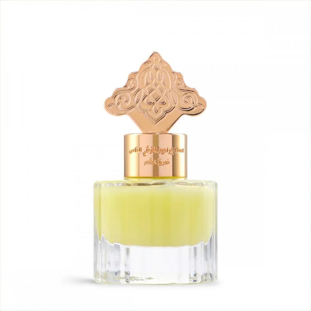  The image depicts a transparent perfume bottle with a yellow-colored liquid. The bottle is topped with a gold cap that has an ornate design, which may draw inspiration from Middle Eastern or Islamic art. The neck of the bottle features gold lettering in Arabic, likely indicating the name of the fragrance or the brand. The cap and the color of the liquid give the product a luxurious and exotic appearance, suggesting that it may be a cardamom-scented musk designed for use on hair.