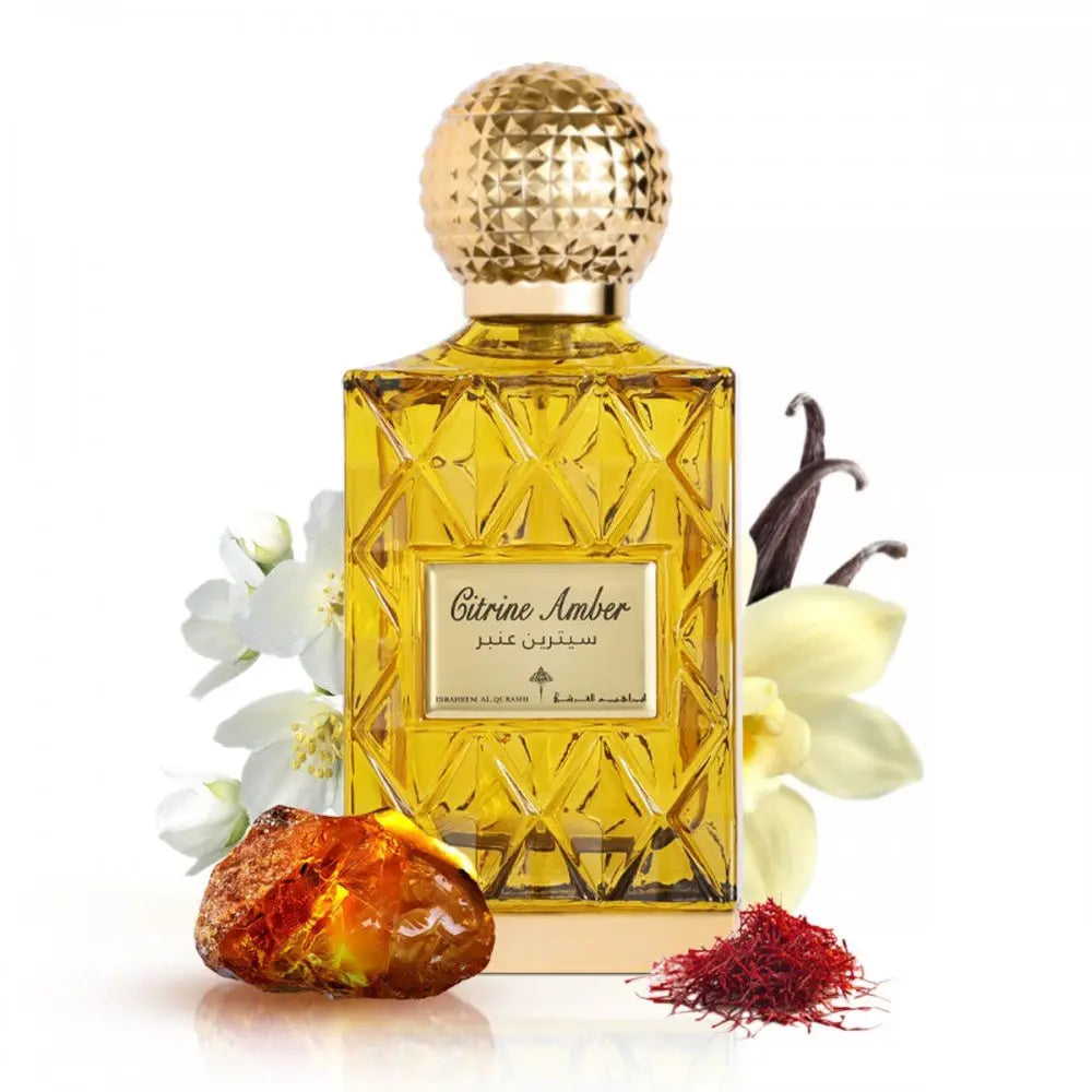 The image depicts a perfume bottle with a golden yellow liquid, named "Citrine Amber." The bottle has a textured gold cap and a label with the name in both English and Arabic script. Surrounding the bottle are a piece of amber resin, a few saffron threads to the right, vanilla pods to the upper right, and white flowers to the left, likely to represent some of the scent notes in the fragrance.