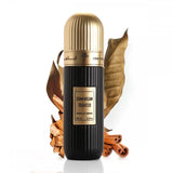 A cylindrical black perfume bottle with a gold cap, labeled "DOMINICAN TOBACCO" in white text, and "Extrait de Parfum 100 ml 3.4 fl.oz" in smaller white text. It has an Arabic inscription and the brand name "IBRAHEEM AL QURASHI" at the top. The bottle is presented in front of two large dried tobacco leaves and rests on a surface with scattered cinnamon sticks. The background is white, emphasizing the product.