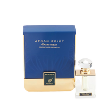 The image shows a perfume product with its packaging. The perfume bottle is clear with a square base and features a golden band around the neck, topped with a large, round, clear cap. The front label is minimalistic, with the name "AFNAN EDICT OUSCTIQUE" in a simple font. Next to the bottle is its box, which is predominantly navy blue with a textured pattern and a broad golden base.  The combination of navy blue and gold suggests a luxurious and sophisticated product.