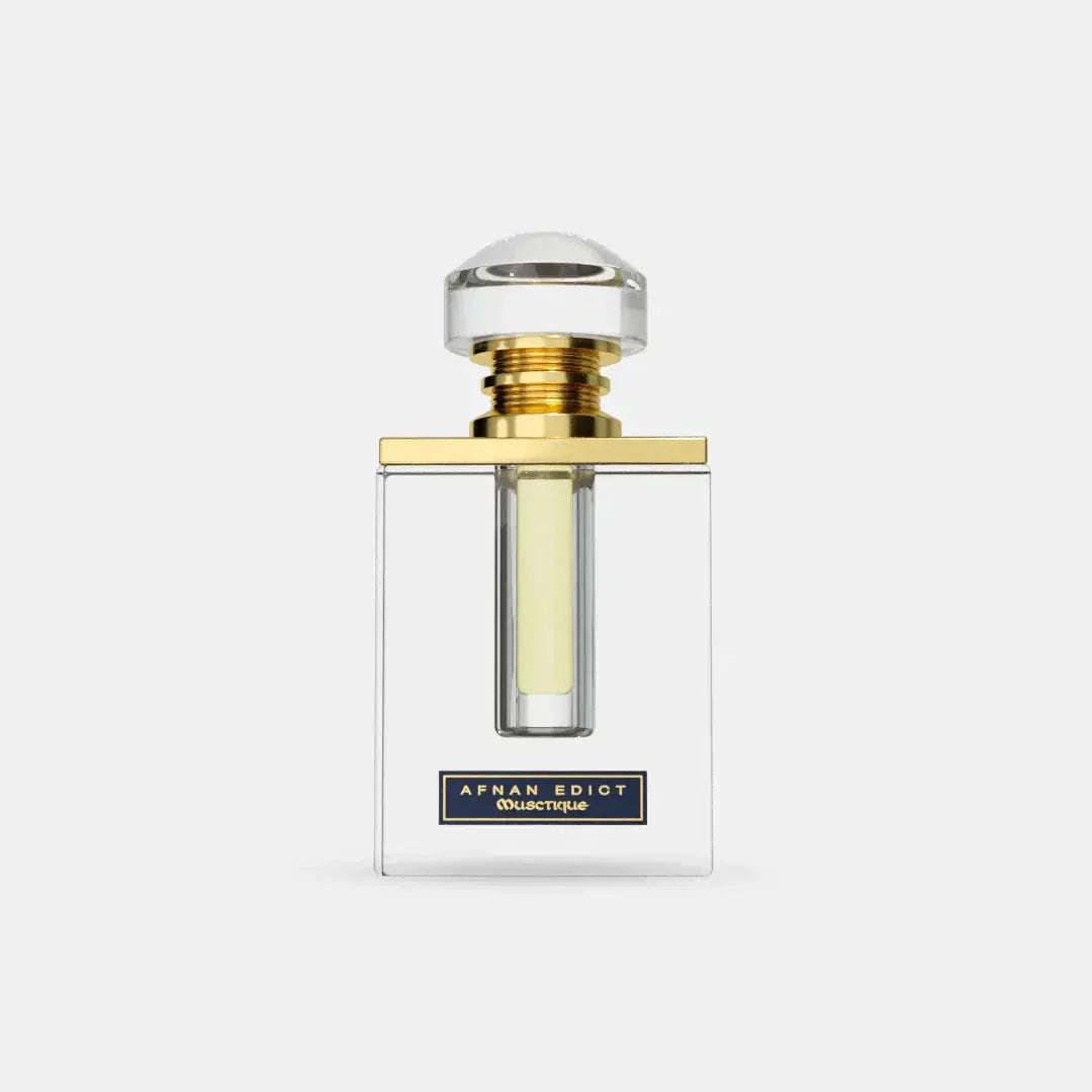 The image features a clear glass perfume bottle with a simple, elegant design. The bottle has straight lines with a rectangular body, allowing the light yellow-colored perfume inside to be visible. It is topped with a large, round cap that appears to be made of crystal-clear material, mounted on a gold band that adds a touch of luxury.