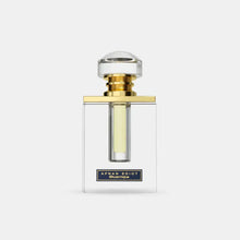 The image features a clear glass perfume bottle with a simple, elegant design. The bottle has straight lines with a rectangular body, allowing the light yellow-colored perfume inside to be visible. It is topped with a large, round cap that appears to be made of crystal-clear material, mounted on a gold band that adds a touch of luxury.