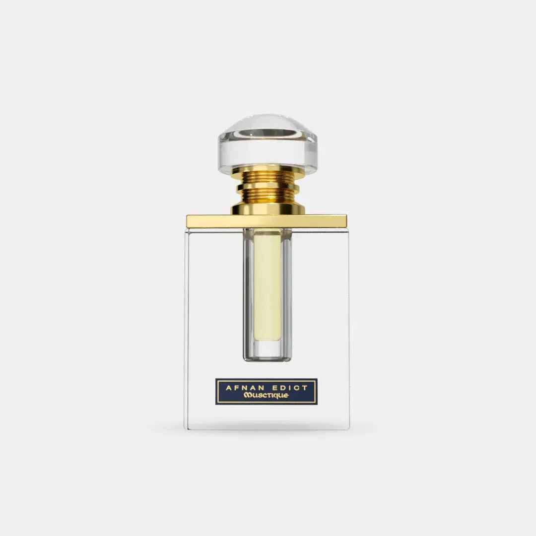 The image features a clear glass perfume bottle with a simple, elegant design. The bottle has straight lines with a rectangular body, allowing the light yellow-colored perfume inside to be visible. It is topped with a large, round cap that appears to be made of crystal-clear material, mounted on a gold band that adds a touch of luxury.