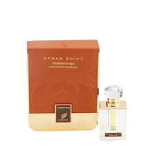 The image shows a perfume product consisting of a rectangular glass bottle and its packaging. The bottle, placed to the right, has a clear liquid with a golden neck and a large, transparent, faceted cap. On its front, there's a label with "AFNAN EDICT Ouddiction" in black letters on a gold background. To the left is the box, in a gradient of brown to gold with a subtle paisley design, and it reads "AFNAN EDICT Ouddiction CONCENTRATED PERFUME OIL" in gold embossed letters. 