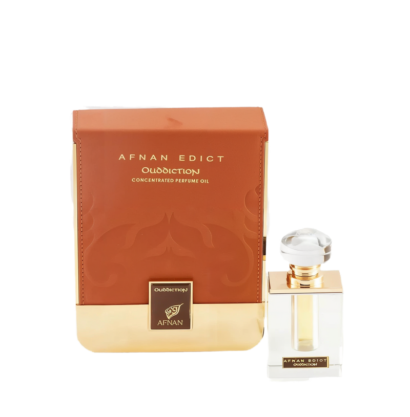 The image shows a perfume product consisting of a rectangular glass bottle and its packaging. The bottle, placed to the right, has a clear liquid with a golden neck and a large, transparent, faceted cap. On its front, there's a label with "AFNAN EDICT Ouddiction" in black letters on a gold background. To the left is the box, in a gradient of brown to gold with a subtle paisley design, and it reads "AFNAN EDICT Ouddiction CONCENTRATED PERFUME OIL" in gold embossed letters. 