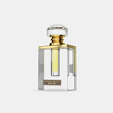 The image is of a transparent glass perfume bottle with a clear liquid inside. The bottle has a rectangular body with beveled edges and a thick base, giving it a luxurious appearance. The cap is a large, clear, faceted piece resembling a cut gemstone, mounted on a gold-colored neck. There is a label on the bottle with the text "AFNAN EDICT Ouddiction" in black letters on a gold background. The overall design is elegant and modern.