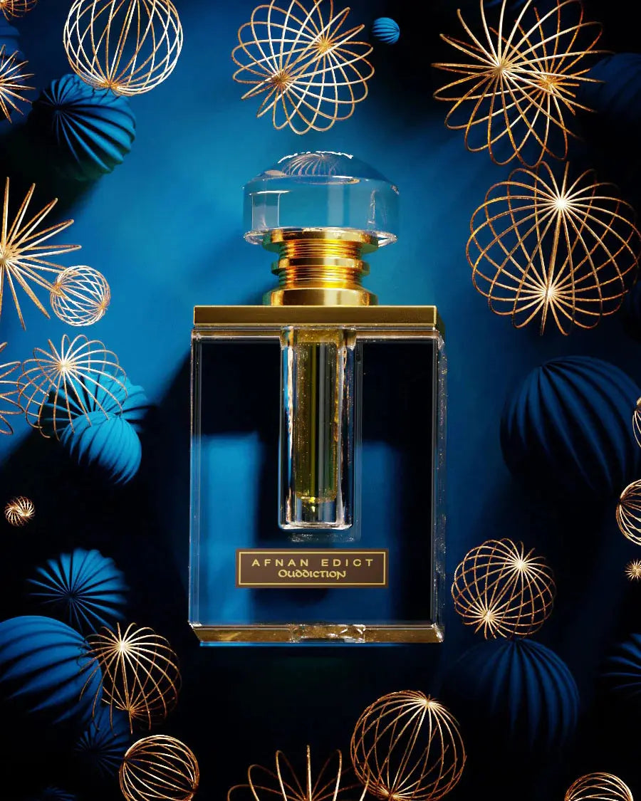 The image features an elegant perfume bottle prominently displayed against a dark blue background adorned with golden wireframe spheres that resemble festive ornaments. The bottle has a clear, rectangular shape with a thick base, enhancing its luxurious appearance. The cap is a large, transparent, faceted piece that resembles a cut gemstone, and it sits atop a golden neck, creating a striking contrast with the deep blue backdrop. 