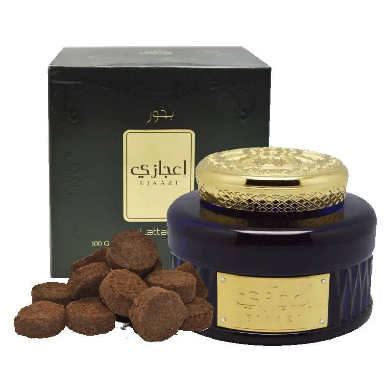 This is an image of a dark blue jar with a decorative golden lid, next to a black box with gold and white accents, labeled "Ejaazi" in Arabic and English. Next to the jar are several brown bakhoor incense tablets. The product is identified as bakhoor, a type of fragrant incense typically used in the Middle East, and the presentation suggests it is from the brand Ard Al Zaafaran.