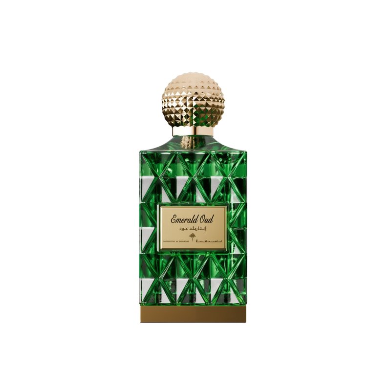 A luxurious bottle of Emerald Oud perfume by Ibraheem Al-Qurashi, featuring a geometric emerald green glass design with reflective triangular facets. The bottle is topped with a textured, spherical gold cap and has a gold nameplate on the front engraved with 'Emerald Oud' in elegant script along with Arabic text and branding. A solid gold base completes the opulent look, conveying a rich and sophisticated aesthetic.