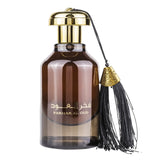 A translucent brown bottle with a gold cap, featuring Arabic script that reads "Fakhar Al Oud" along with the English translation below. An ornamental tassel with a gold-colored decorative top is attached to the neck of the bottle, adding to the luxurious presentation of this oud fragrance. The product is likely a high-end perfume or essential oil, commonly used in Middle Eastern scents.