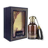 A dark, elegant perfume bottle with "Fakhar Al Oud" written in Arabic calligraphy and a tassel decoration, alongside a matching box with a window revealing the bottle. The box has "THE PRIDE OF OUD" printed on it, indicating that the fragrance contains the luxurious and prized oud scent. The packaging is ornate, hinting at the rich and traditional essence of the perfume inside.