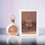 An elegant white perfume bottle with rose gold accents and a cap featuring Arabic calligraphy stands next to its packaging. The front of the bottle is adorned with a rose gold butterfly emblem and the name "Fakhar Lattafa" embossed below it. The box has a sophisticated rose gold design with intricate arabesque patterns and the text "Fakhar Lattafa" and "Pride of Lattafa" on it.