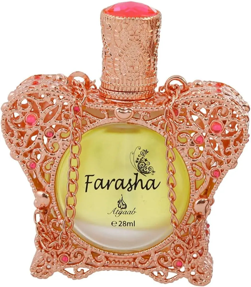 A close-up of an ornate perfume bottle with a rose gold lace-like design embellished with pink gemstones. The bottle cap is textured and also in rose gold, with a peach-colored top. It contains a yellow liquid, and the front of the bottle has the name "Farasha" printed in black, with a small butterfly motif above it, and "Ayyashi e 28ml" indicating the fragrance volume.