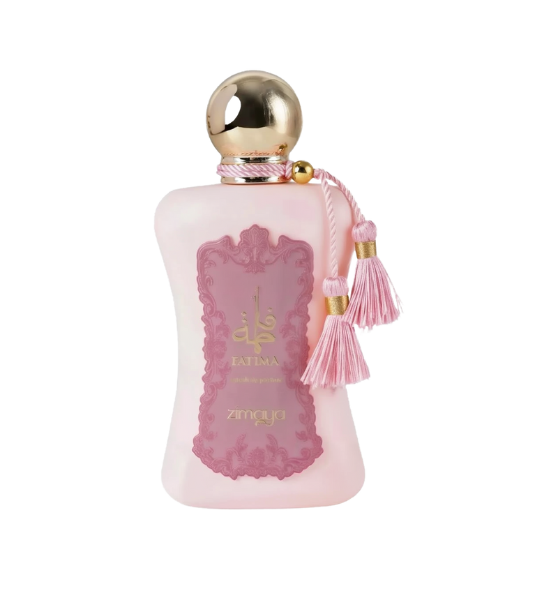 The image shows a bottle of "Fatima" extrait de parfum by Zimaya. The perfume bottle is an elegant, soft pink color with a gold spherical cap. It features a pink label with ornate detailing and gold text, reading "Fatima" in both English and Arabic, along with "extrait de parfum" and the brand name "zimaya" at the bottom. The bottle is adorned with two pink tassels hanging from the neck, adding a touch of luxury and sophistication.