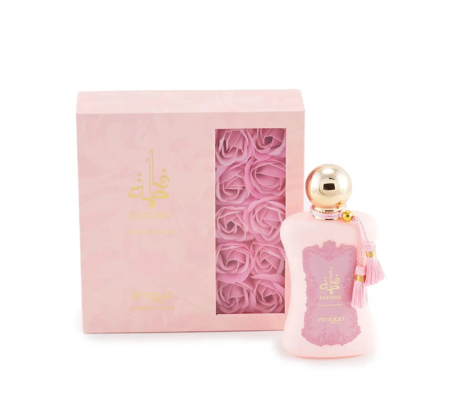 The image shows a bottle of "Fatima" extrait de parfum by Zimaya alongside its packaging. The perfume bottle is a soft pink color with a gold spherical cap and is adorned with pink tassels. It features a pink label with ornate detailing and gold text that reads "Fatima" in both English and Arabic, along with "extrait de parfum" and the brand name "zimaya" at the bottom. The accompanying box is also pink with gold text and a clear window showcasing pink rose petals inside.