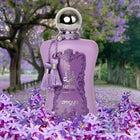 The image shows a bottle of "Fatima Velvet Love" extrait de parfum by Zimaya set against a background of a lavender field with trees. The perfume bottle is a soft lavender color with a silver spherical cap and is adorned with matching lavender tassels. It features a lavender label with ornate detailing and silver text that reads "Fatima" in both English and Arabic, along with "Velvet Love," "extrait de parfum," and the brand name "zimaya" at the bottom. 