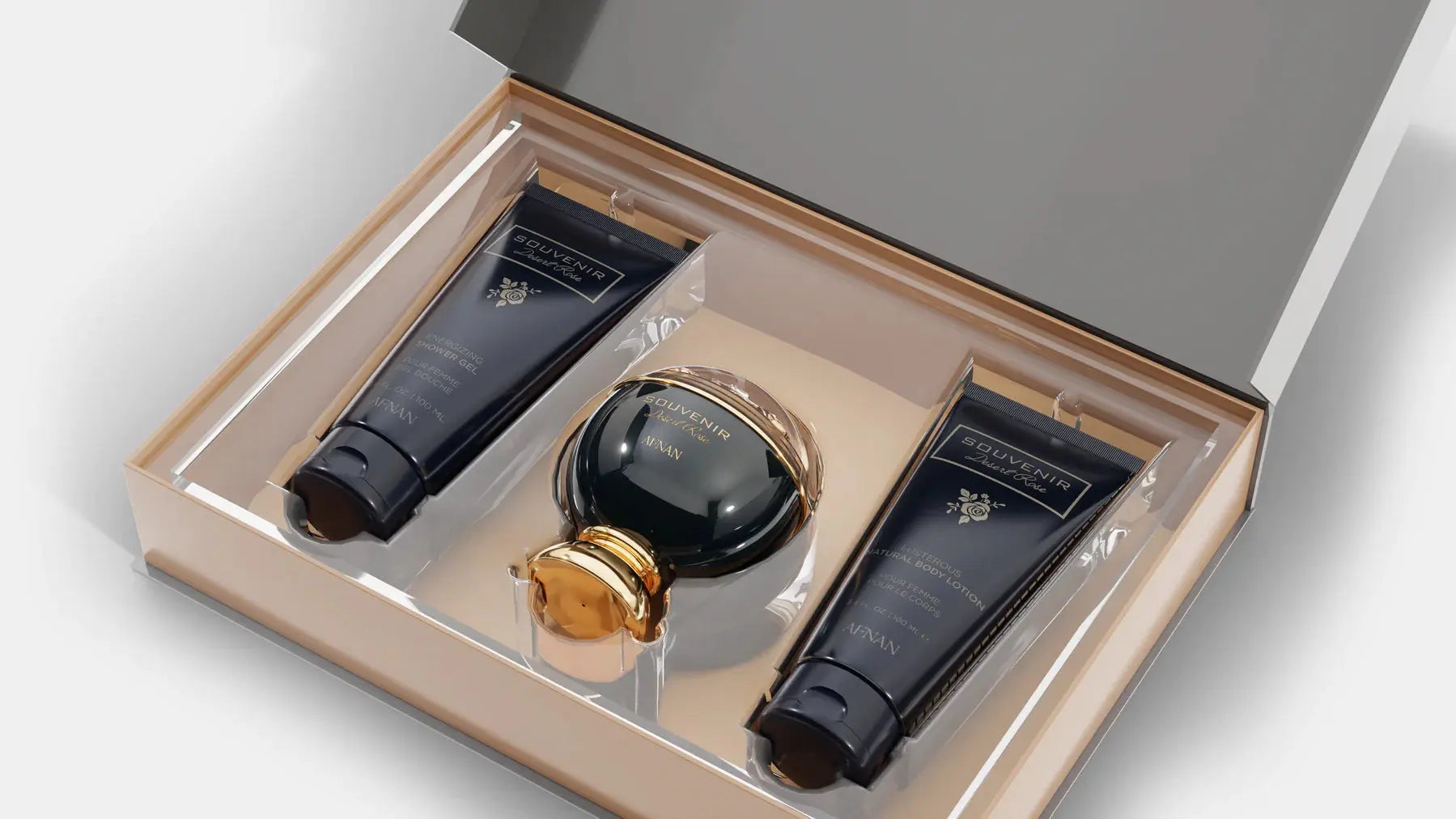 The image shows an elegant gift set by Afnan Perfumes from their "SOUVENIR Desert Rose" collection. The set is displayed in a beige presentation box with a clear lid, revealing its contents. Inside, there is a dark, glossy perfume bottle with a spherical design and a golden cap, positioned centrally. On either side of the perfume bottle are two matching dark tubes.  Both tubes and the perfume bottle feature the "SOUVENIR Desert Rose" branding in elegant gold lettering