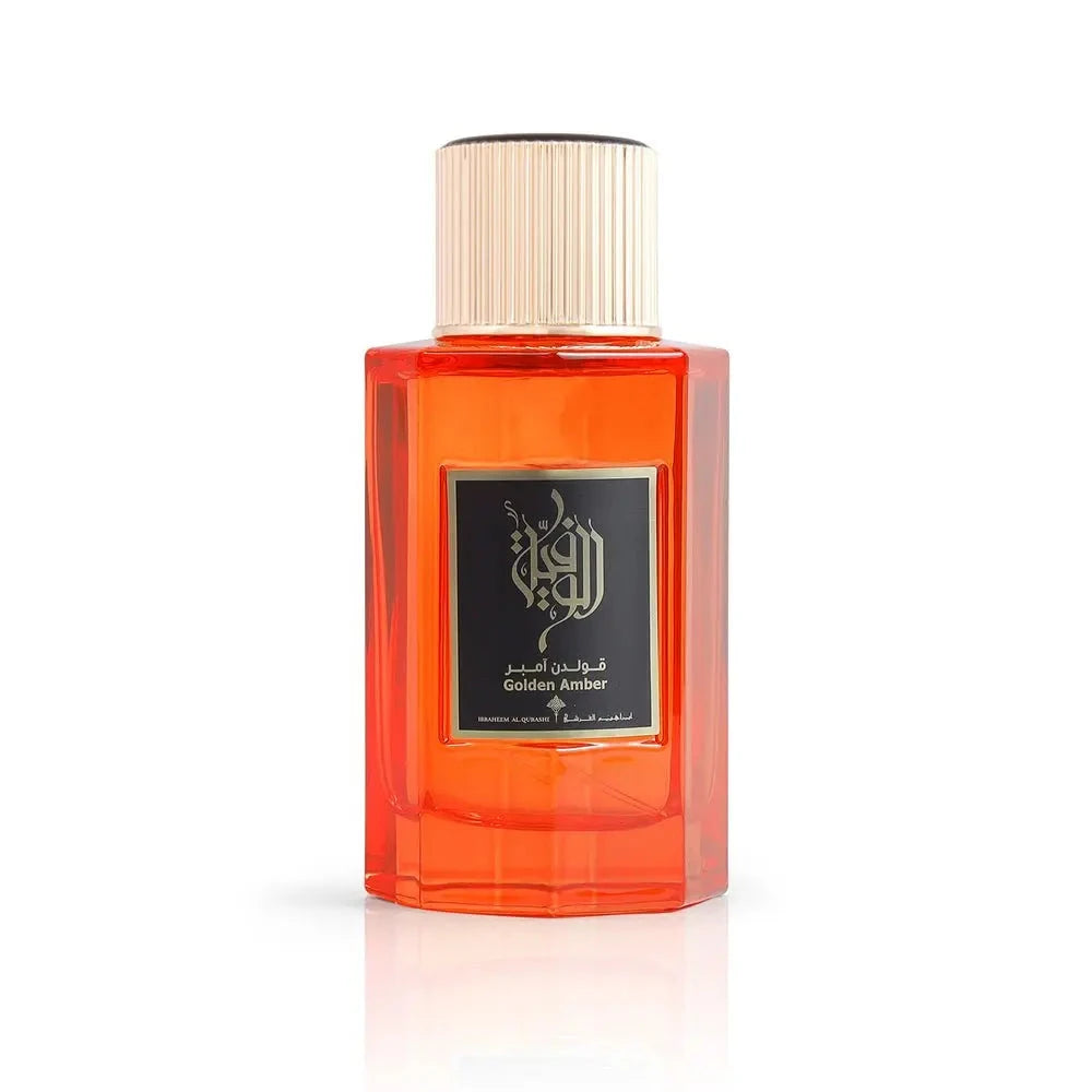 This is an image of a rectangular, transparent orange perfume bottle with a white cap. The front of the bottle has a black label with golden Arabic calligraphy and the English words "Golden Amber" beneath it. The bottle is presented against a plain white background, highlighting the vibrant orange color of the perfume liquid inside.