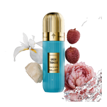 A visually striking presentation of Greek Tobacco Extrait De Parfum by Ibraheem Al-Qurashi. The vertically ribbed light blue bottle with a metallic gold dome cap is surrounded by splashes of water and key fragrance elements, including white orchid petals, pink lychee, a pale rose blossom, and creamy resin. The gold nameplate on the bottle displays 'GREEK TOBACCO' and product details in bold black text. The dynamic black background highlights the freshness and luxurious composition of the scent.