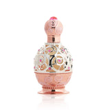 The image depicts an ornate perfume bottle on a white background. The bottle features a rose gold base and cap with intricate swirl patterns embossed on the surface. A decorative metal overlay with filigree designs encases the clear central portion of the bottle, adorned with small pink gemstone accents. The cap is topped with a pink crystal-like element, adding to the luxurious appearance of the bottle.