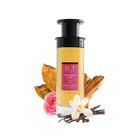 This is an image of a cylindrical clear perfume bottle with a black pump and a yellowish liquid inside, labeled "RT Happiness Dose" with additional text in Arabic and "ROSE TOBACCO" underneath. The bottle is positioned against a white background with a pink rose, a dry tobacco leaf, a cluster of vanilla beans, a white orchid flower, and some cinnamon sticks arranged around it, indicating the scent notes of the perfume.
