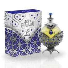 A close-up of the Hareem Al Sultan Blue perfume bottle by Khadlaj. The bottle is elaborately decorated with silver and blue accents, featuring a teardrop shape with a blue jewel in the center. The silver detailing around the bottle includes intricate patterns and designs, giving it a regal and antique appearance.