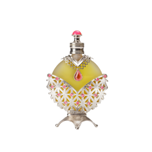 A round perfume bottle with a yellowish-green liquid, adorned with intricate silver and pink detailing, including a red teardrop-shaped gemstone at the center and a silver cap with a pink top.