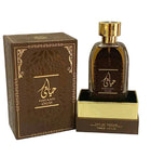 n image of Hayaati Oud perfume by Ard Al Zaafaran, featuring the perfume bottle and packaging. The bottle is transparent with a dark amber liquid and a reflective gold cap. It sits on a gold-colored base with the text "EAU DE PARFUM NATURAL SPRAY 100ml e 3.4fl.oz" at the bottom. The brown box has an ornate design with golden accents and Arabic calligraphy, along with the name "HAYAATI OUD" in both Arabic and English.
