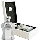 The image displays a luxurious perfume set featuring a sleek, silver bottle with a textured design and a regal-looking crest labeled "Highness" on the front. The bottle has a shiny silver cap and is presented in an open white box with a black quilted interior, which adds to the elegance of the product. A matching accessory, possibly a perfume applicator or a smaller bottle, rests beside the main perfume bottle inside the box. 