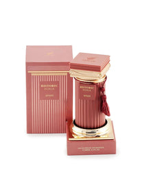 The image shows a luxurious perfume product. The perfume bottle is placed on a podium-like stand with a reflective golden surface. The bottle is cylindrical with ribbed texture and a rich, rosy pink hue. It features a golden cap adorned with a decorative tassel in a matching rosy pink color. The label on the bottle reads "HISTORIC DORIA AFNAN". Beside the bottle is its packaging box, which follows the same color scheme and has vertical stripes, with the brand and perfume name printed on it. 