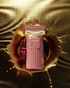 The image showcases a luxurious perfume bottle from the Afnan "Historic Doria" collection against a shimmering gold background with a dynamic splash of golden liquid surrounding it. The perfume bottle is a sophisticated pink with a ribbed texture, reminiscent of classical columns. A deep pink tassel adds a touch of opulence to the presentation. The bottle is labeled with "HISTORIC DORIA" and the Afnan brand name in an elegant font.