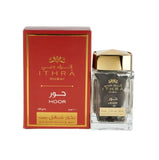 The image shows a product against a white background. On the right is a rectangular clear glass perfume bottle with a golden cap. The bottle contains a dark-colored liquid and has Arabic script and the word "HOOR" printed in gold lettering. On the left is a rectangular red box with gold and white Arabic script, the name "ITHRA DUBAI" in English at the top, and "HOOR" just below it. 