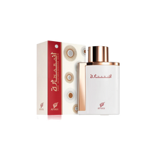 The image showcases a perfume bottle and its packaging. The bottle has a flat, rectangular shape with rounded edges, featuring a glossy white finish and a metallic rose gold cap. The front of the bottle displays the perfume's name "?????" in elegant red Arabic script, with the "AFNAN" logo in red below. Accompanying the bottle is its box, which has a white background with geometric circular patterns and a bold red side panel where the perfume's name and brand logo are repeated in white and red.