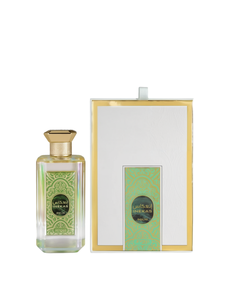 A bottle and packaging of Inekas Solis Eau De Parfum by Zimaya. The perfume bottle is made of clear iridescent glass with a geometric shape, adorned with a gold hexagonal cap and an ornate green and gold label featuring Arabic and English text. The elegant white box is framed with gold trim and includes a matching green and gold patterned design on the front.