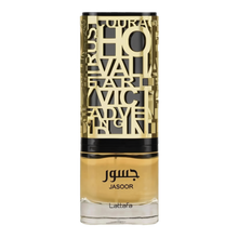 The image shows a bottle of perfume. The bottle has a clear bottom filled with yellow-amber colored liquid, presumably the fragrance. It features a detailed, ornate, gold-colored metallic overlay with cut-out letters and designs, and a black band towards the top, under the cap. The name "JASOOR" is prominently displayed in the middle of the bottle, with the brand "Lattafa" written at the bottom. The overall design suggests a luxurious and perhaps Middle Eastern-inspired aesthetic.