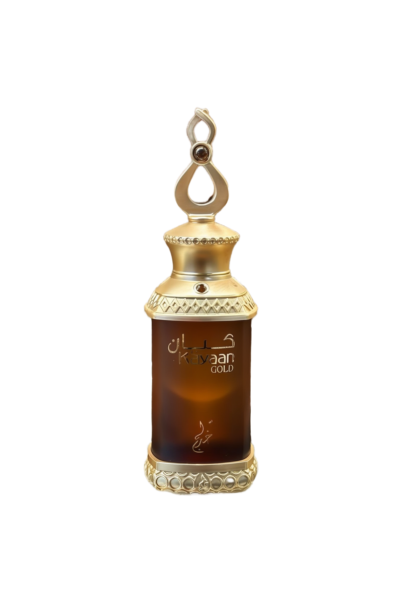 This image features a perfume bottle labeled "Kayaan Gold" resting on a glass surface. The bottle has a regal design with a gold-toned cap adorned with decorative elements and a loop on top, suggesting it can be used as a pendant or for easy carrying. The dark amber liquid inside indicates the perfume might have a rich and possibly woody or oriental fragrance.