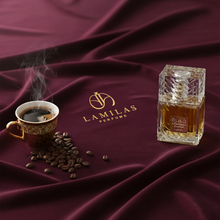 Lattafa Khamrah Qahwa perfume bottle beside steaming coffee cup on burgundy fabric.
