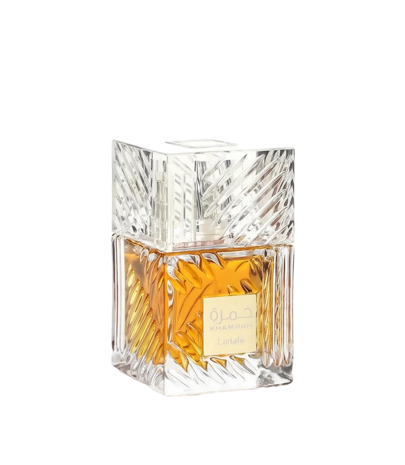 This image displays a square-shaped perfume bottle with a clear crystal-like design. The bottle has a substantial, geometrically cut glass structure that reflects light, enhancing the rich golden-yellow color of the perfume inside. The cap is a clear cube