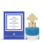 This image shows a square-shaped perfume bottle with a blue to clear gradient and a decorative gold cap, positioned in front of its packaging. The package is blue with a framed white label that includes Arabic calligraphy, the words "BLUEBERRY MUSK," and "IBRAHEEM ALQURASHI SPECIAL" in English. The logo of Ibraheem Al Qurashi is also visible at the bottom of the package.