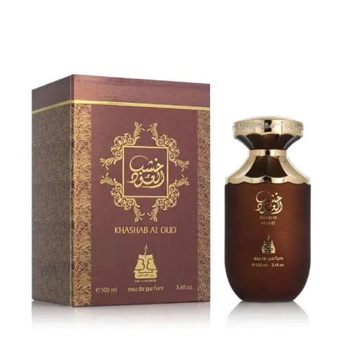 The image shows a bottle of "Khashab Al Oud" perfume by Bait Al Bakhoor alongside its packaging. The perfume bottle has a rounded body with a dark brown gradient and a golden neck, capped with a shiny metallic lid. The front of the bottle displays the name of the perfume in Arabic calligraphy in gold, set against the dark brown background. 