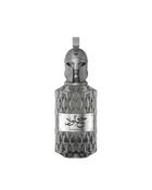 A product shot of Le Falcone Niche Collection’s “Khulood” perfume bottle on a white background: a tall, amber-colored glass vessel with a diamond-cut texture and a polished bronze plaque engraved with Arabic calligraphy above the word “Khulood.” The bottle is crowned by an ornate bronze cap sculpted into a stylized warrior’s helmet with a crest-style loop at the top, conveying a luxurious, sculptural aesthetic.